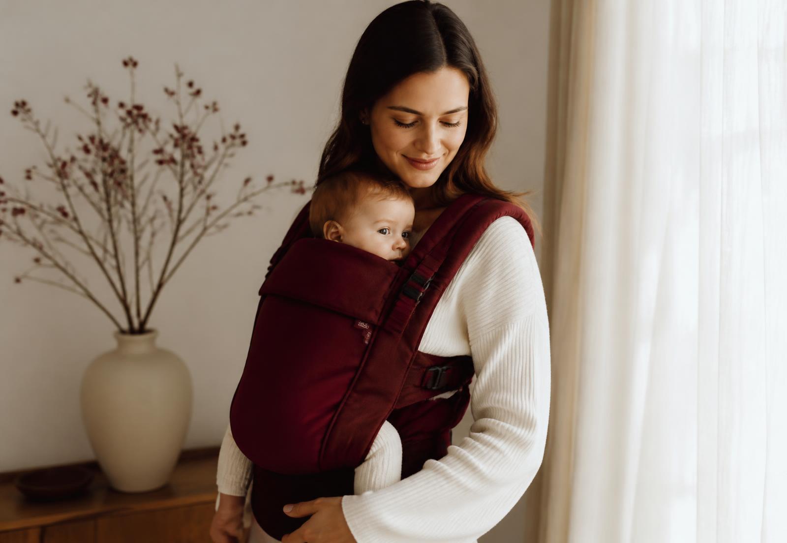 Mother carrying her baby in a burgundy HerChoice carrier